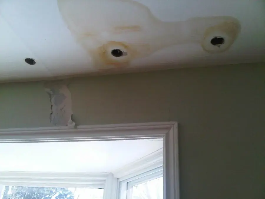 Water stains and opened spots in a ceiling near a window after a leak, ceiling leak damage in Anoka