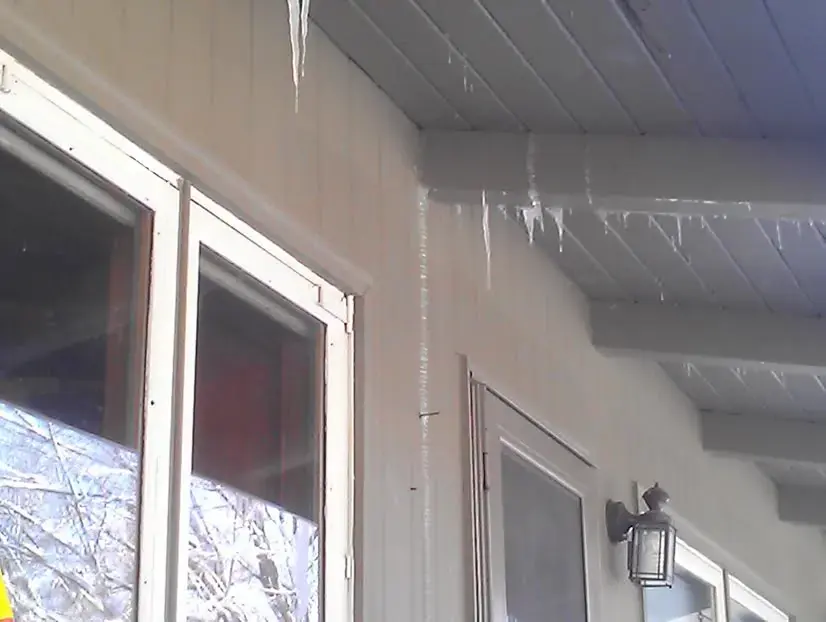 Icicles hanging from a porch roof edge, seen through a window, the kind of cold that tests pipes in older Anoka homes
