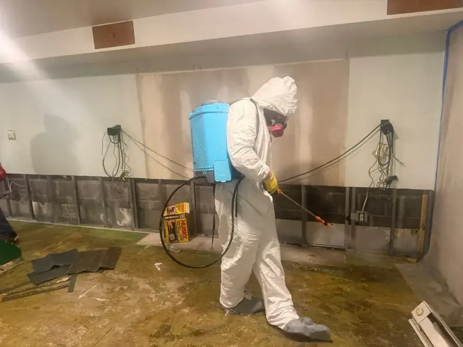 Technician in a protective suit and respirator spraying antimicrobial in a flood-cut basement, sewage cleanup in Anoka